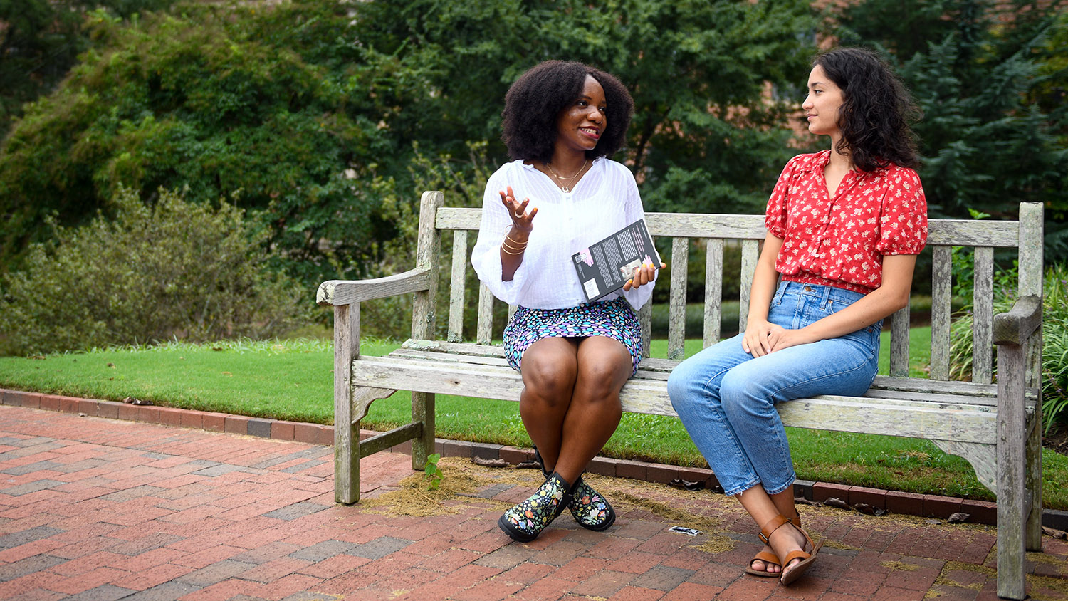 Two graduate students talk on a bench.