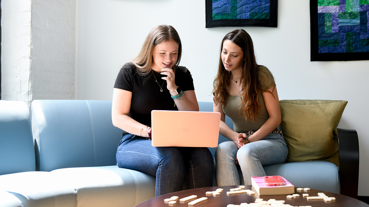 Two students look at a laptop in a lounge.